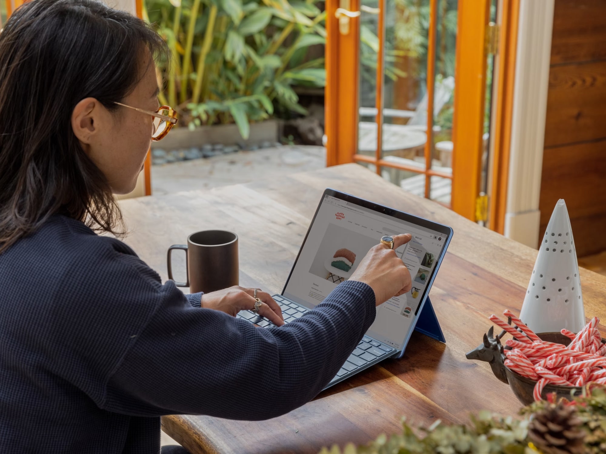 Person working on laptop with coffee mug in cozy, plant-filled workspace