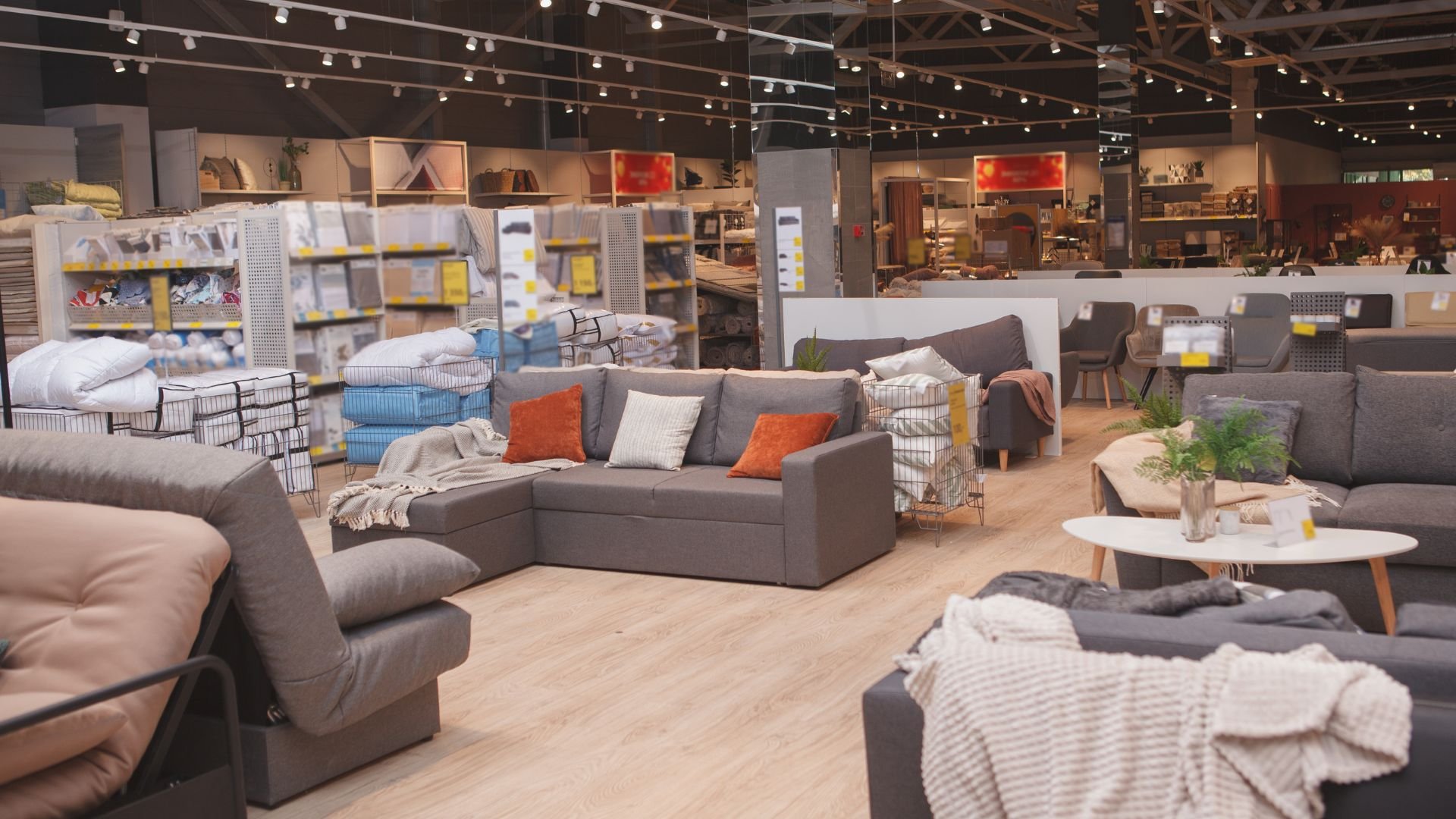 Furniture showroom with grey sofas, orange pillows, and string lights overhead